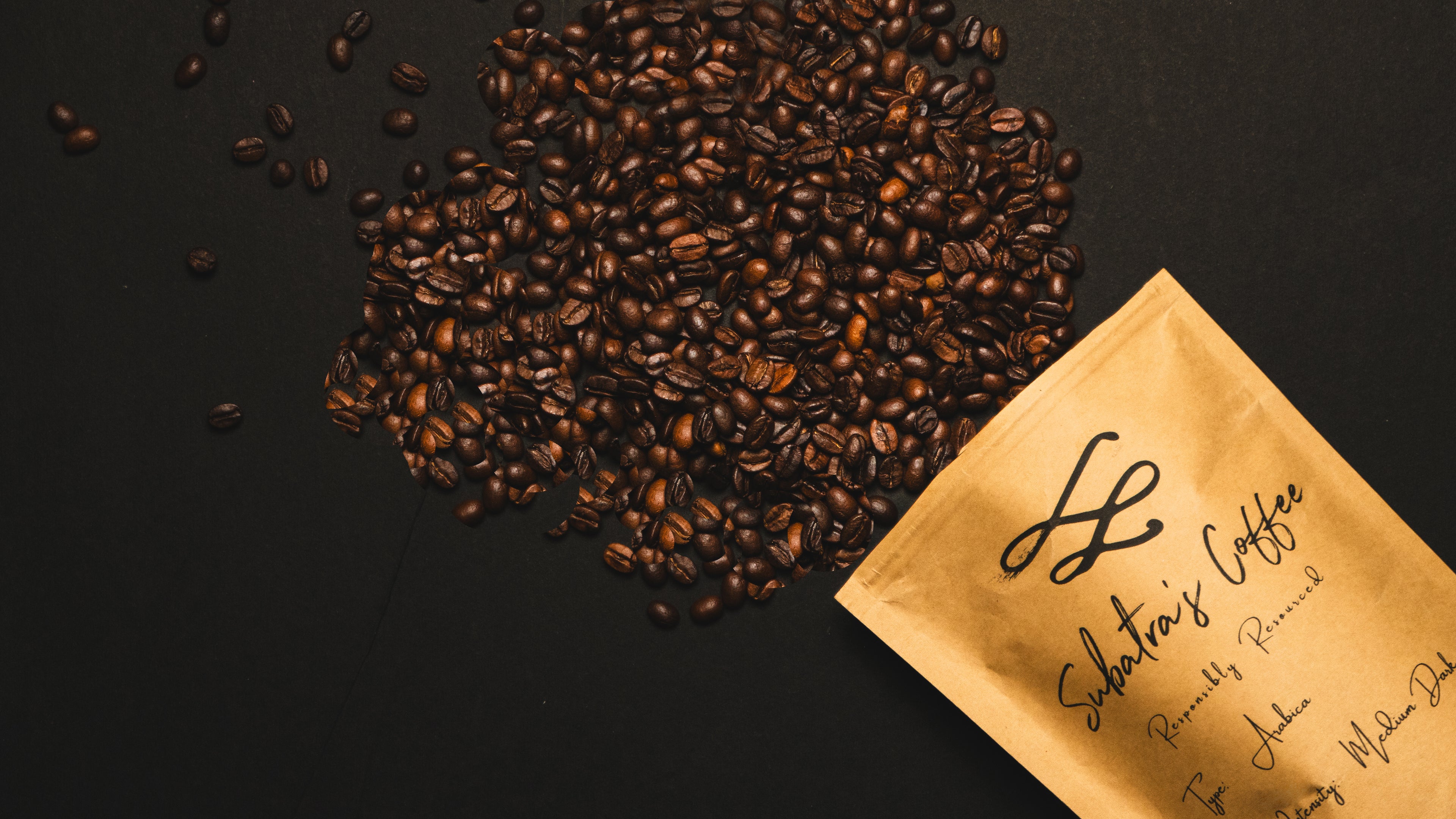 Roasted coffee beans and a branded coffee bag on a dark surface